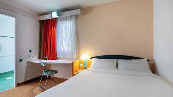 Een hotelkamer met een bed, bureau, stoel en een raam met gordijnen.
