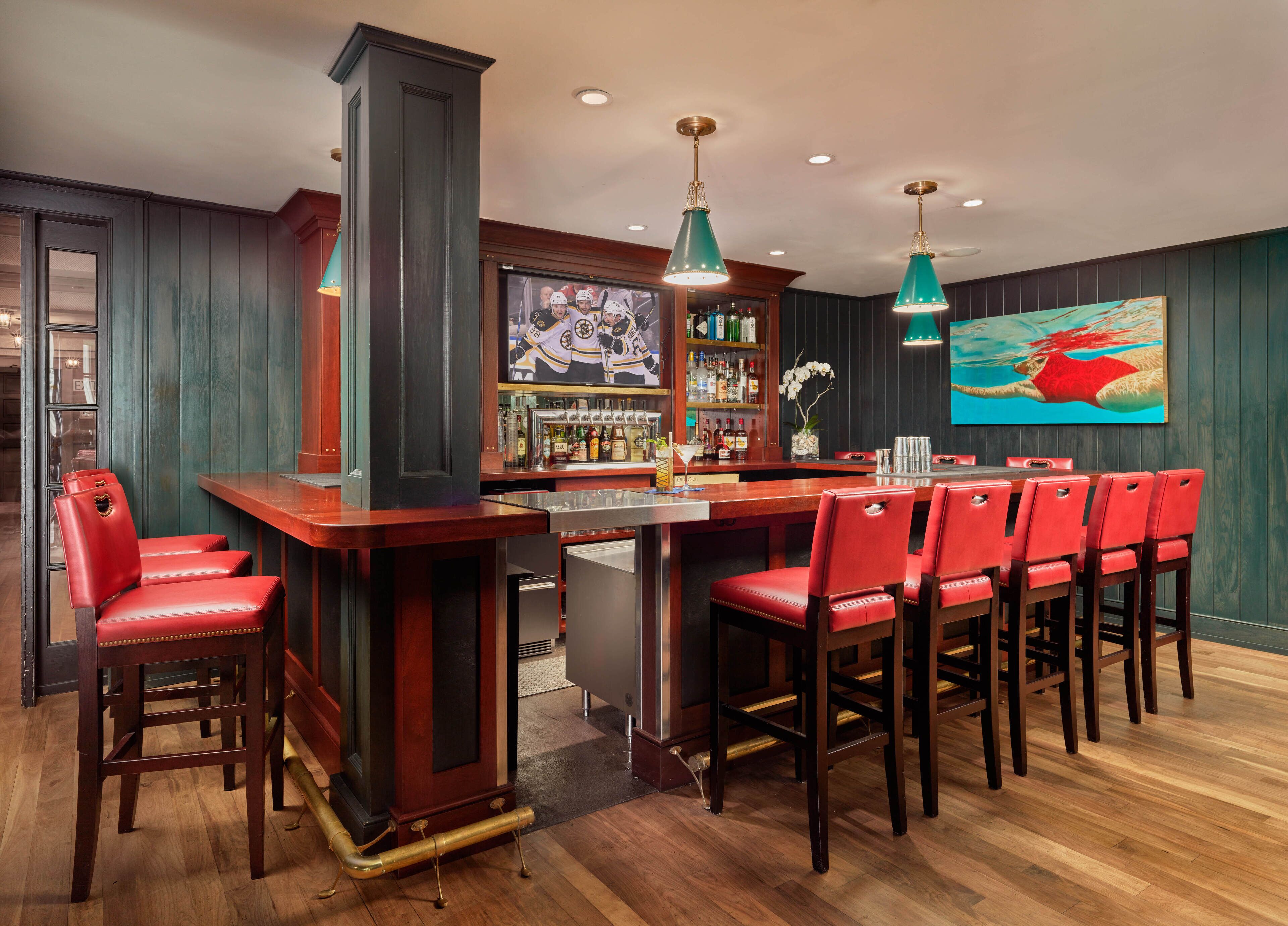A bar area with a long wooden counter, red leather bar stools, and a bar stocked with bottles.