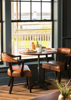 A dining area with a table set for two, featuring a view of a lighthouse through large windows.
