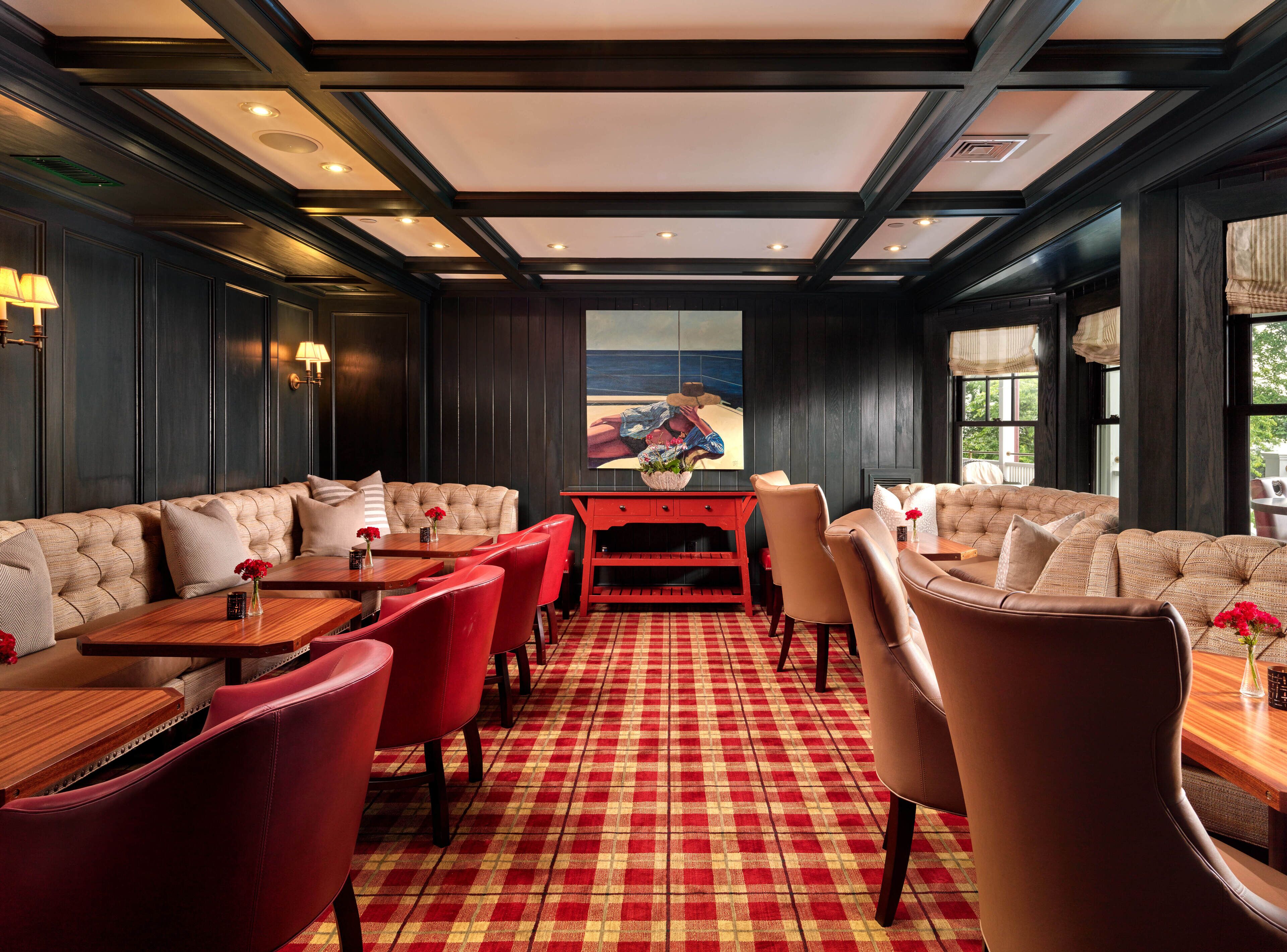 A room with a checkered floor, red and brown leather chairs, a wooden table, and a large window with a view of the outdoors.