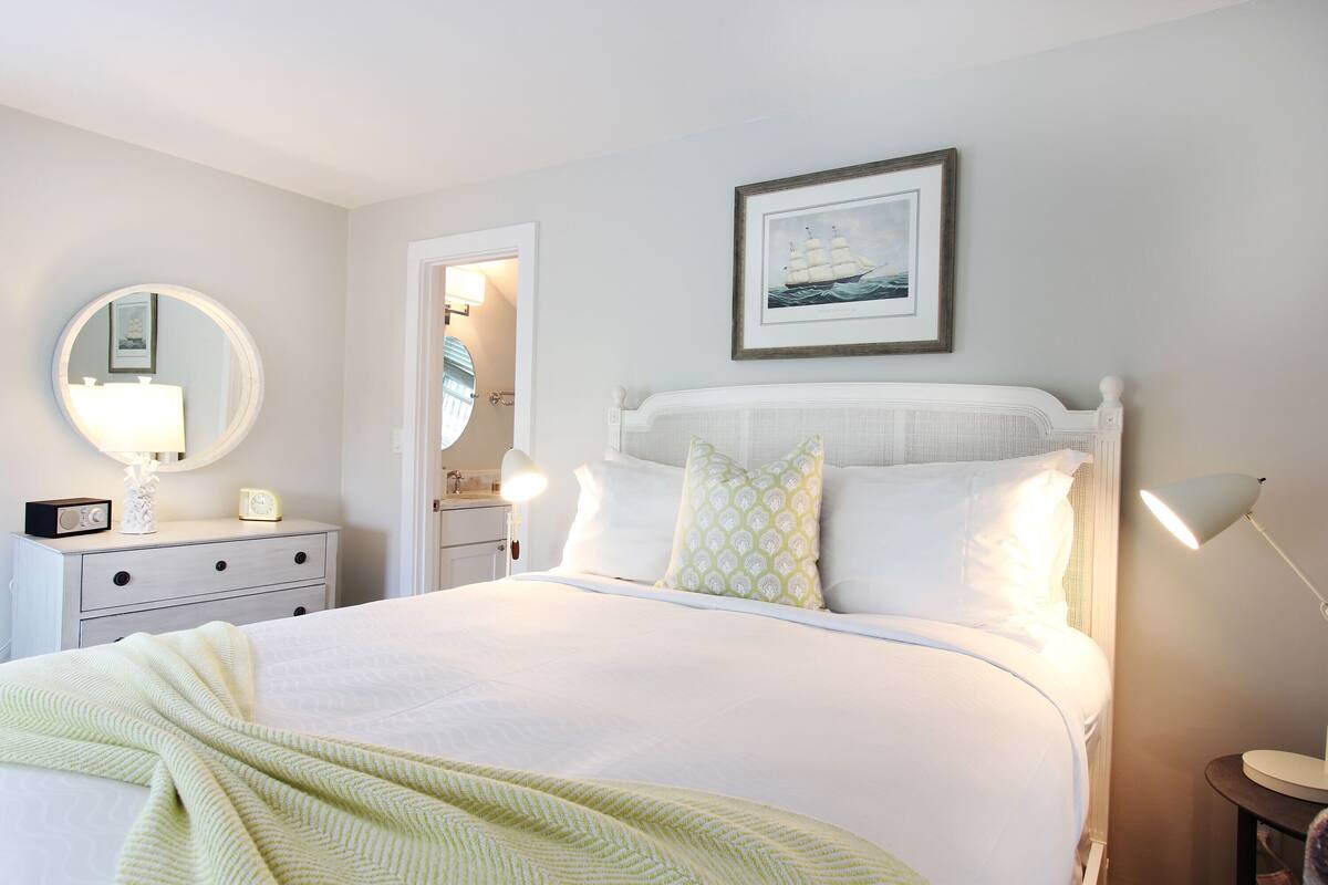 A neatly arranged bedroom with a bed, bedside tables, a mirror, and a framed picture on the wall.