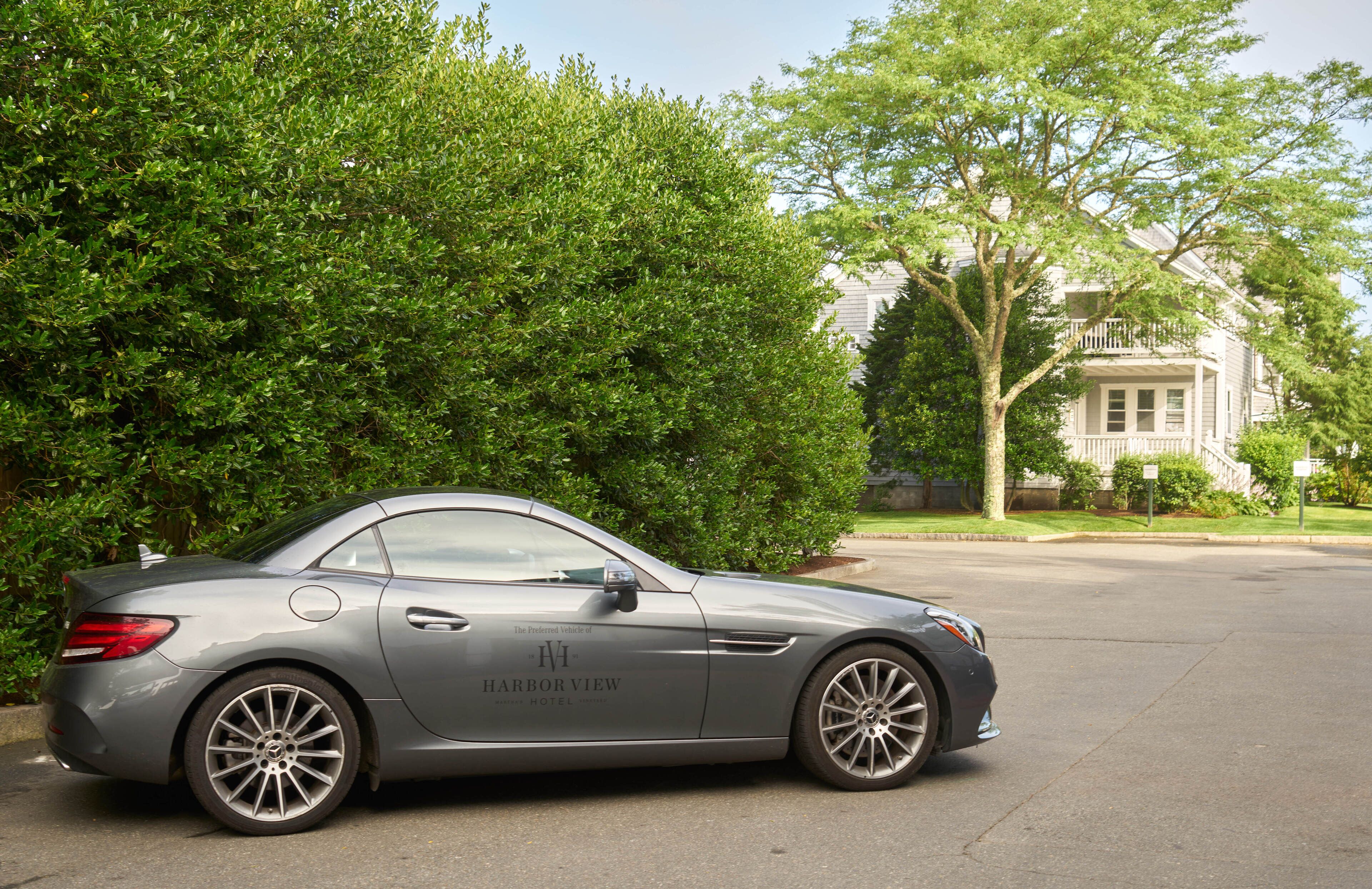 A gray luxury car parked in front of a building with a large tree and a well-maintained lawn.