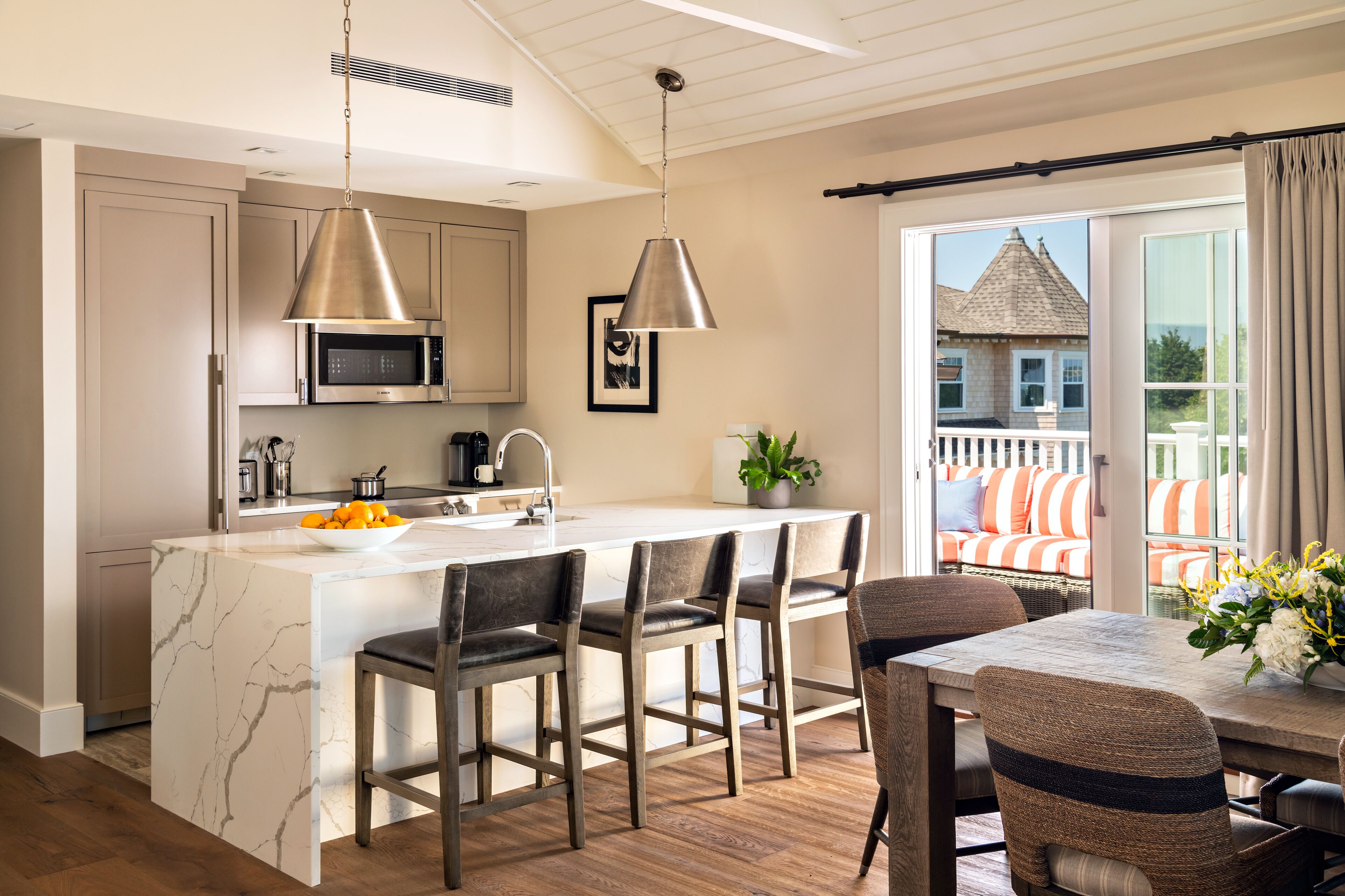 A modern kitchen with a marble island, stainless steel appliances, and a dining area with wicker chairs and a table.