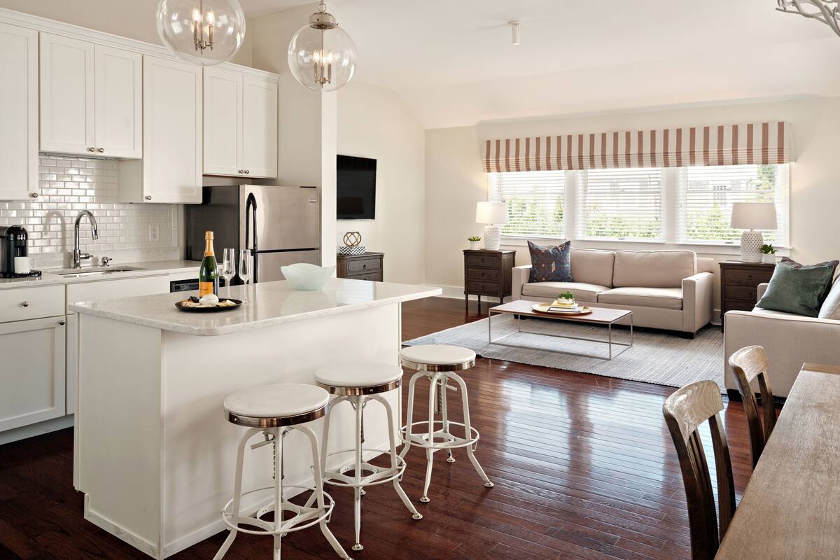 A modern kitchen with white cabinetry, a central island with stools, stainless steel appliances, and pendant lighting.