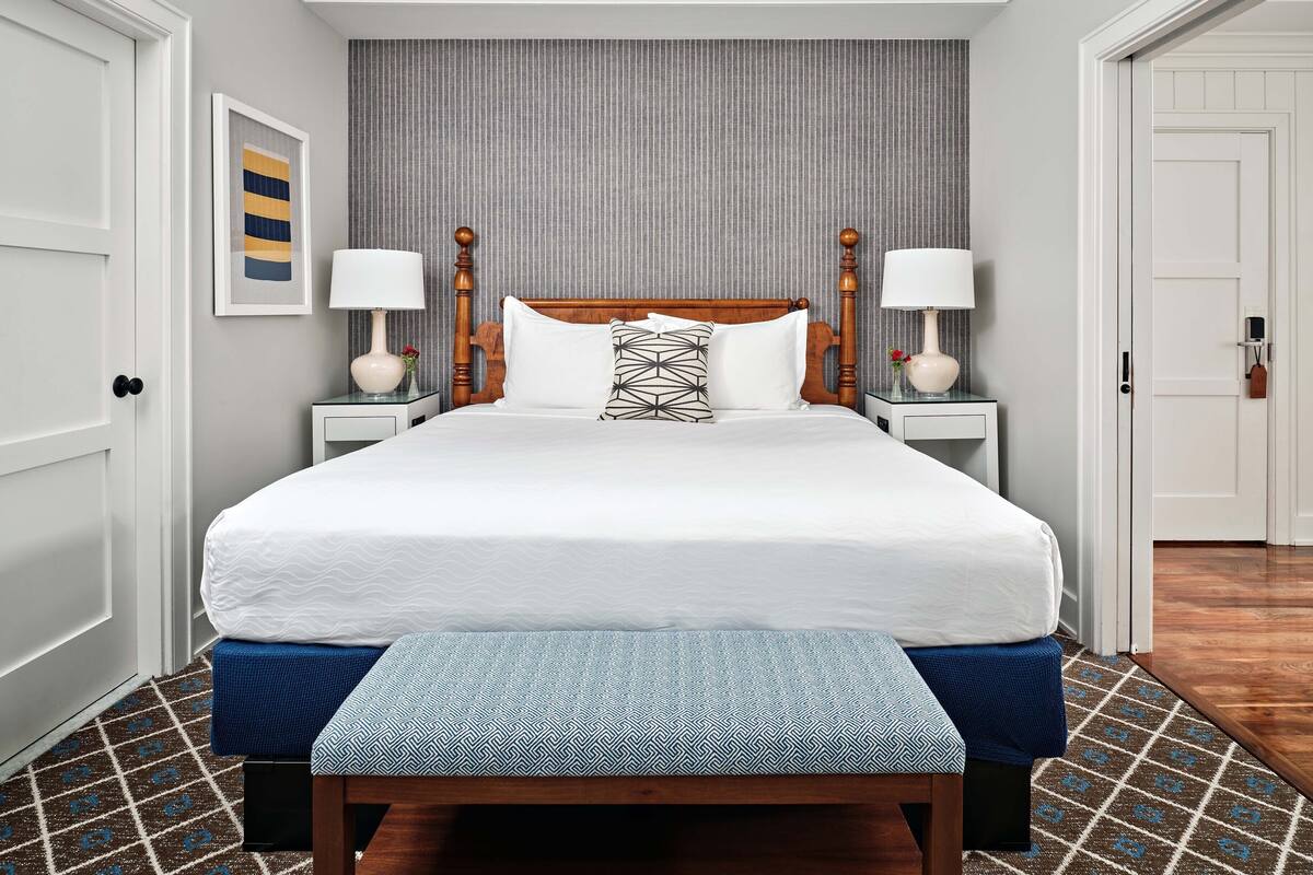 A neatly made bed with a wooden headboard, two bedside lamps, and a patterned rug on a tiled floor.