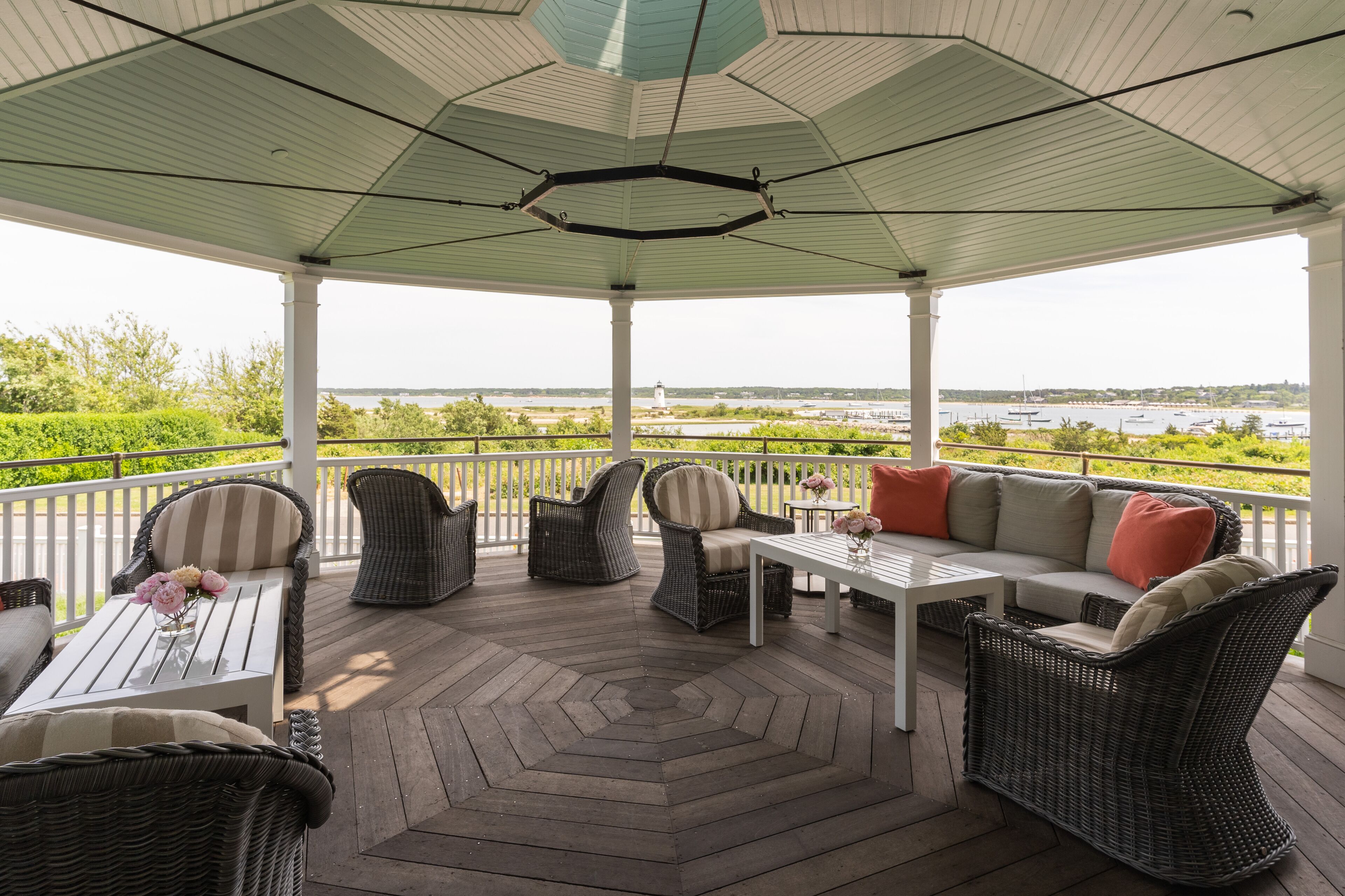 Een overdekt terras met rieten meubilair, een tafel met bloemen en uitzicht op het water en boten.