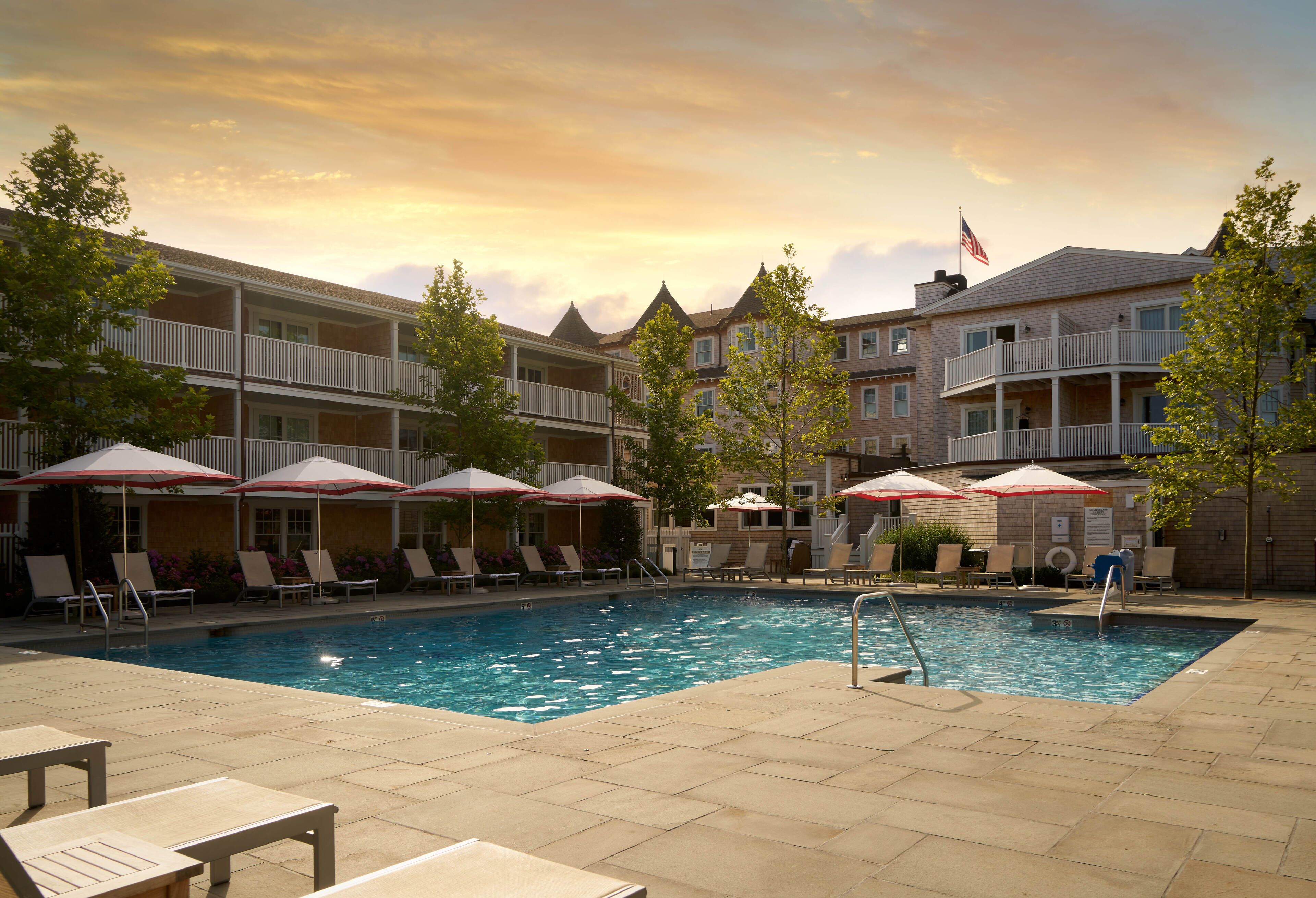 Ein Hotelpoolbereich mit Liegestühlen und Sonnenschirmen, umgeben von mehrstöckigen Gebäuden mit Balkonen.