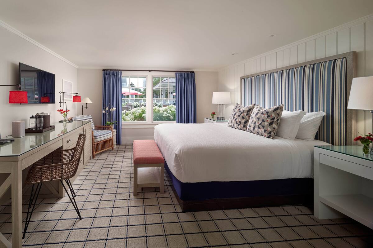 A hotel room with a bed, desk, chair, and a window with curtains.