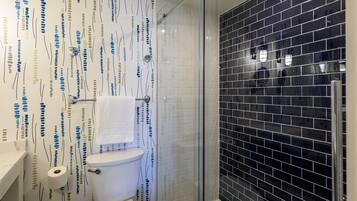 A bathroom with a patterned wall, a toilet, a shower with a glass door, and a sink with a towel hanging on the wall.