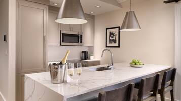 Une cuisine moderne dotée d’un îlot central, d’appareils électroménagers en acier inoxydable et de luminaires suspendus.