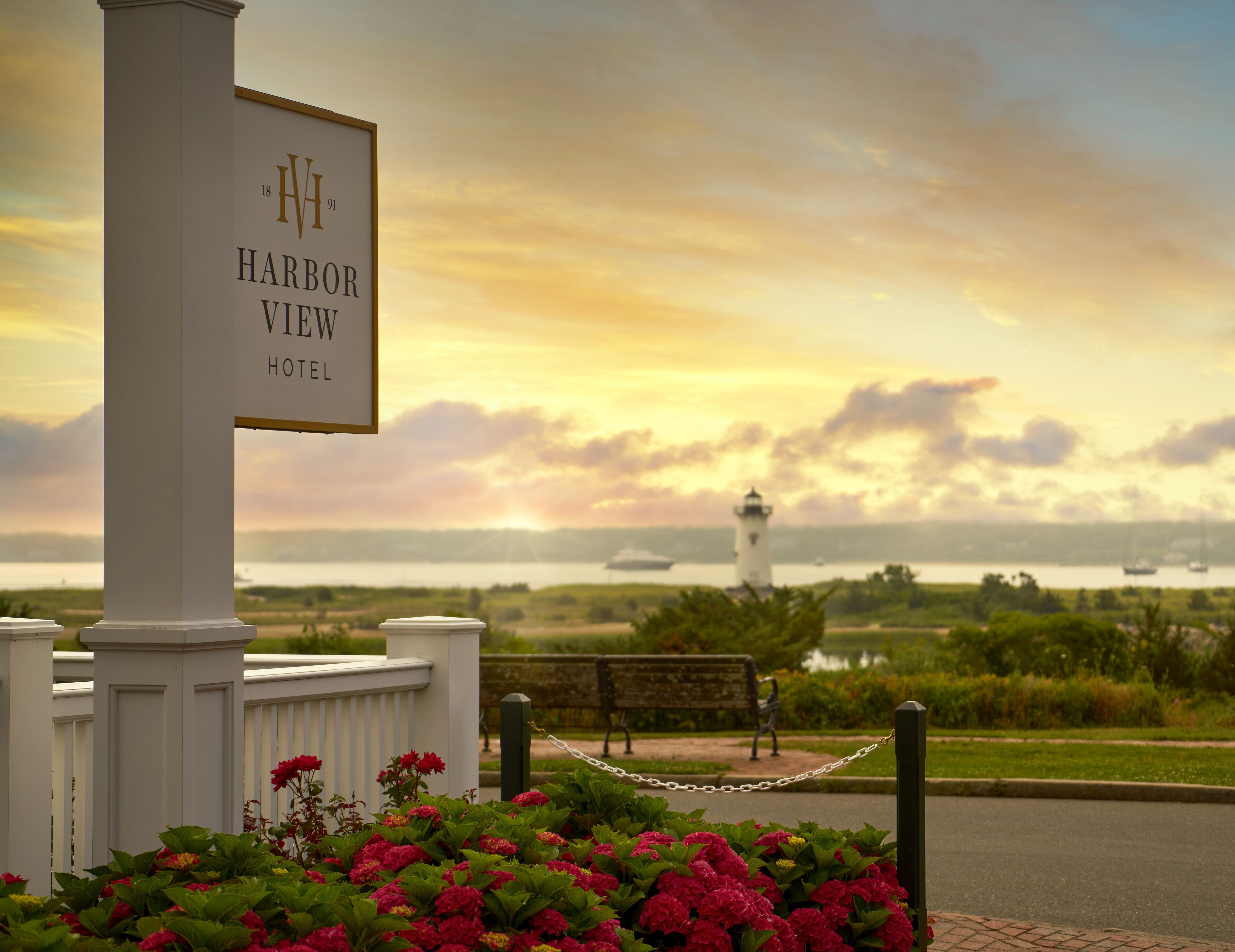 A sign for the Harbor View Hotel with a view of the sea and a lighthouse in the background.