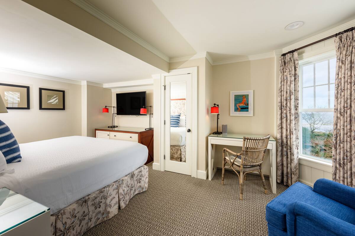 A hotel room with a bed, desk, chair, and a window with curtains.