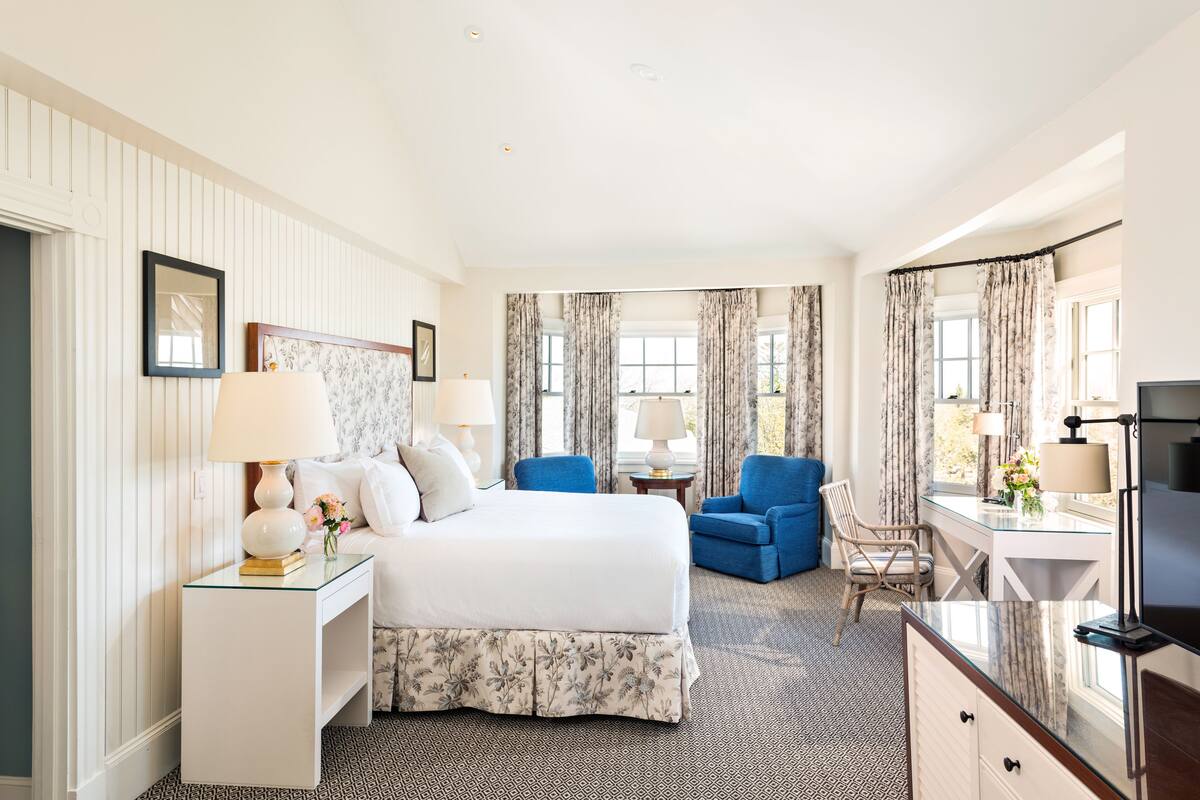 A hotel room with a large bed, two chairs, a desk, and a TV.