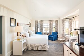 A hotel room with a large bed, two chairs, a desk, and a TV.