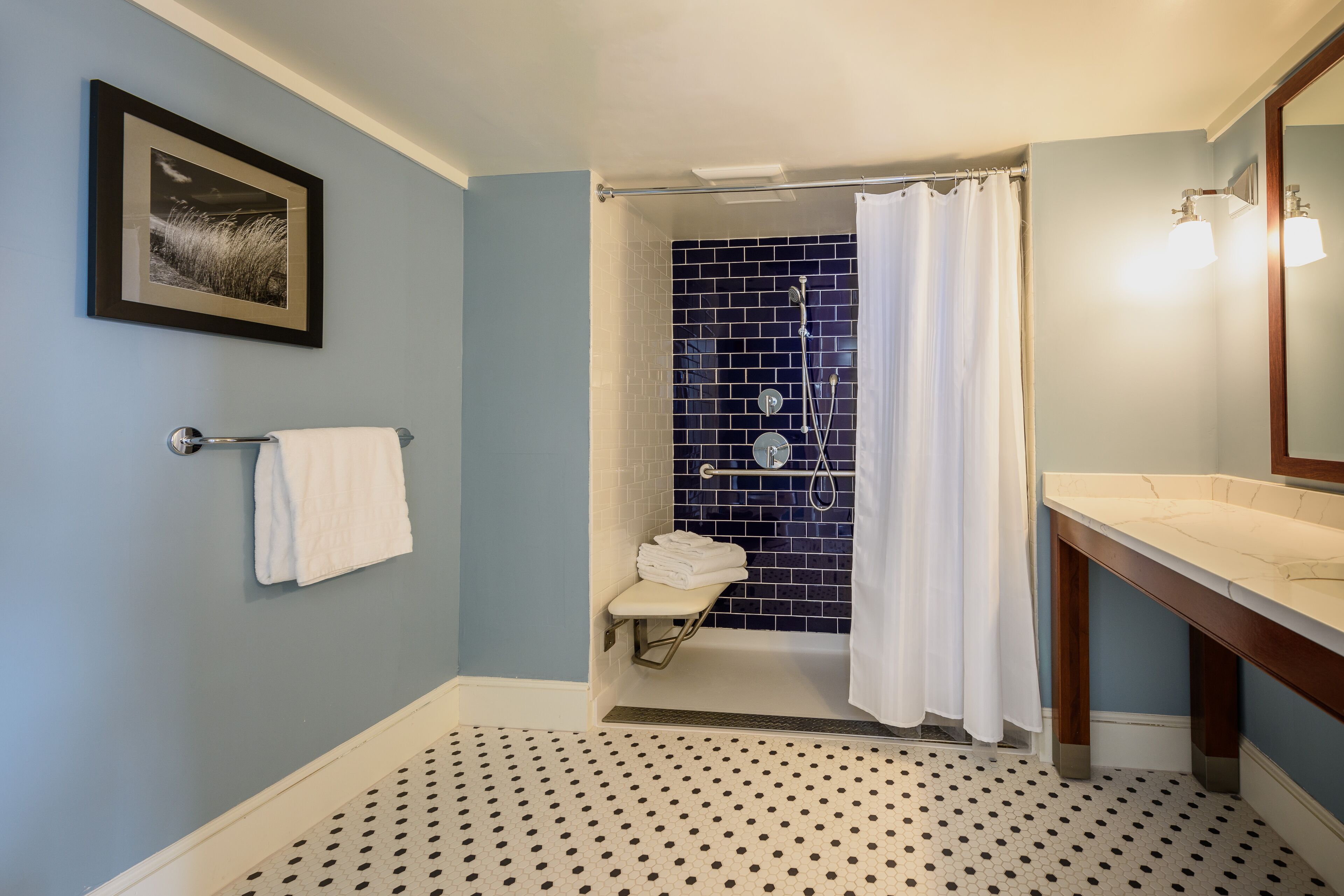 Un baño con ducha, toallero, lavabo e imagen en la pared.
