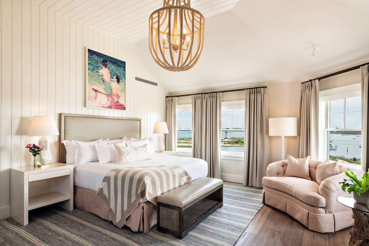 A hotel room with a large bed, a chaise lounge, a painting, and a view of the water.