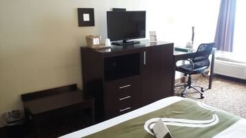 Habitación de hotel con cama, escritorio, silla, televisión y ventana con cortinas.