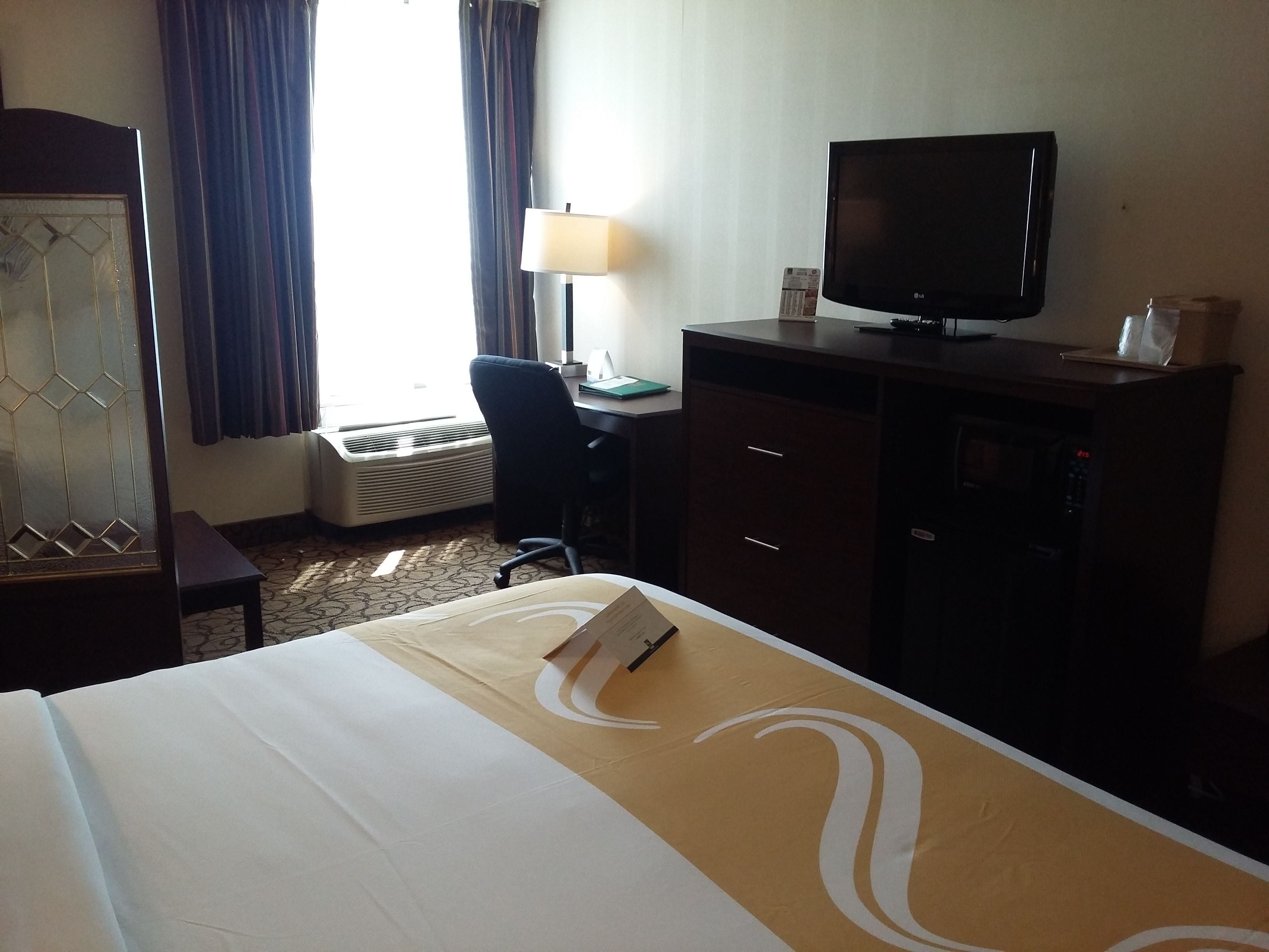 Een hotelkamer met een bed, een bureau, een televisie en een raam met gordijnen.