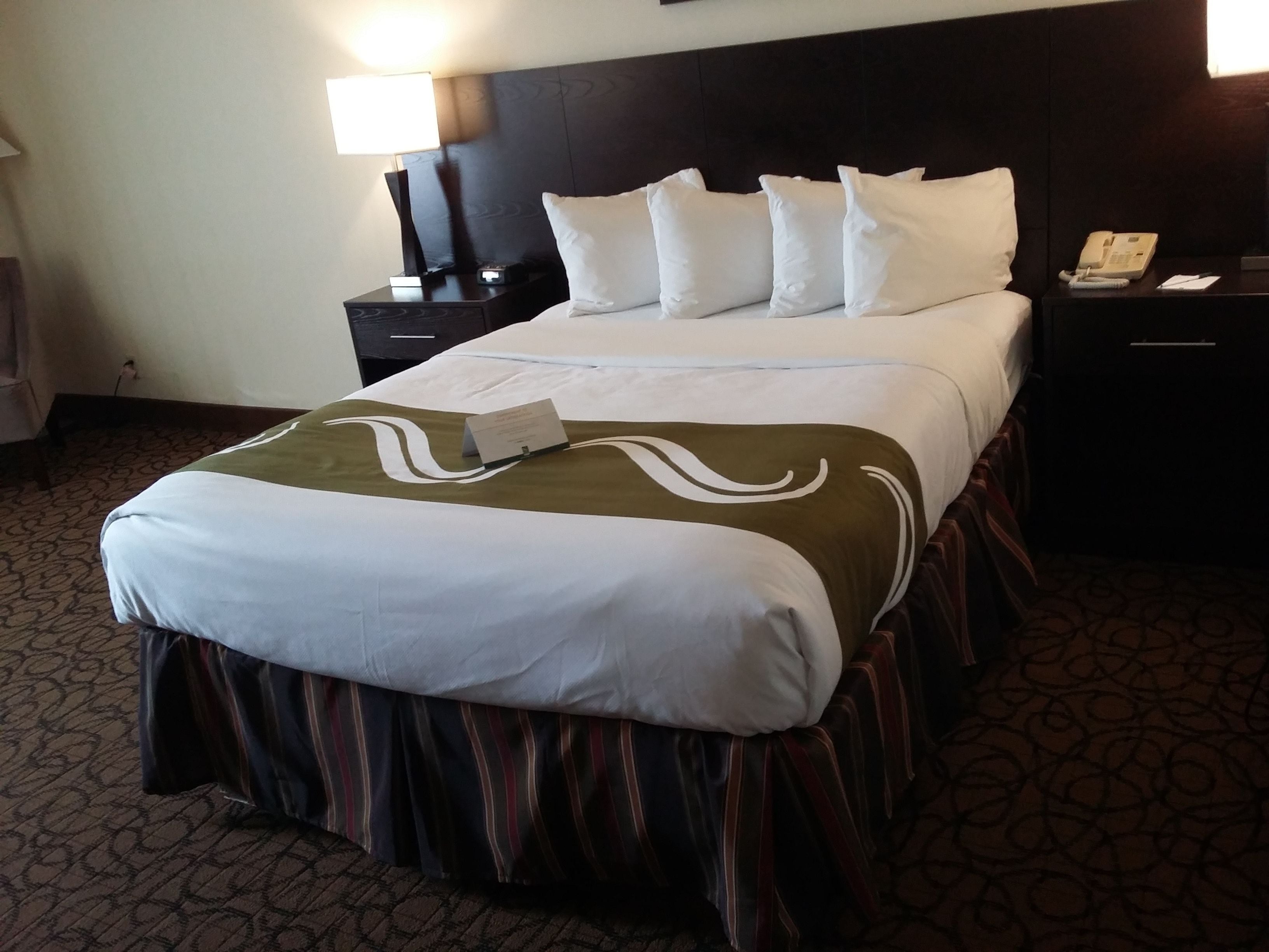 A hotel room with a large bed, a nightstand with a lamp, and a phone.