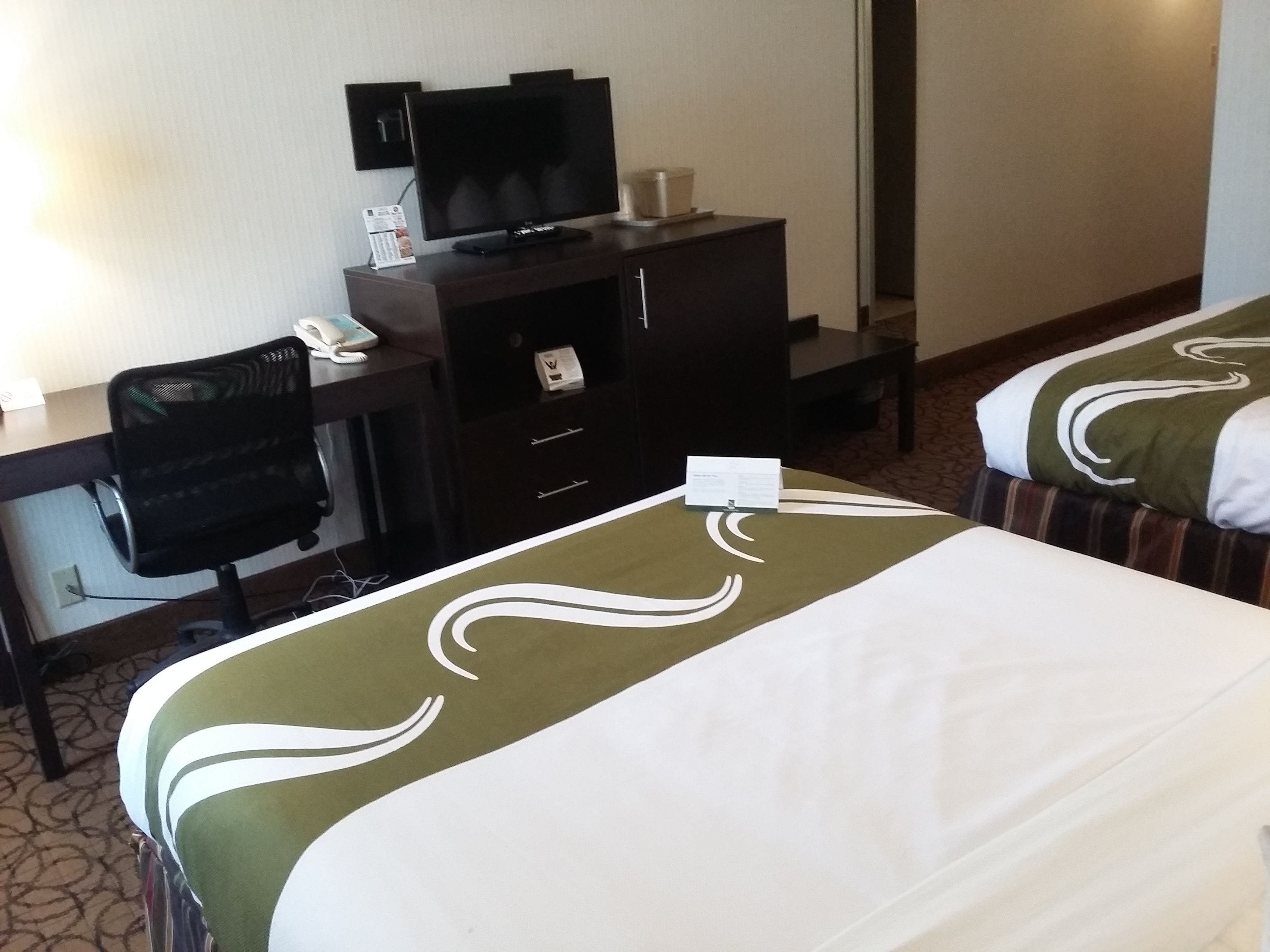 A hotel room with two beds, a desk with a computer and a telephone, and a chair.