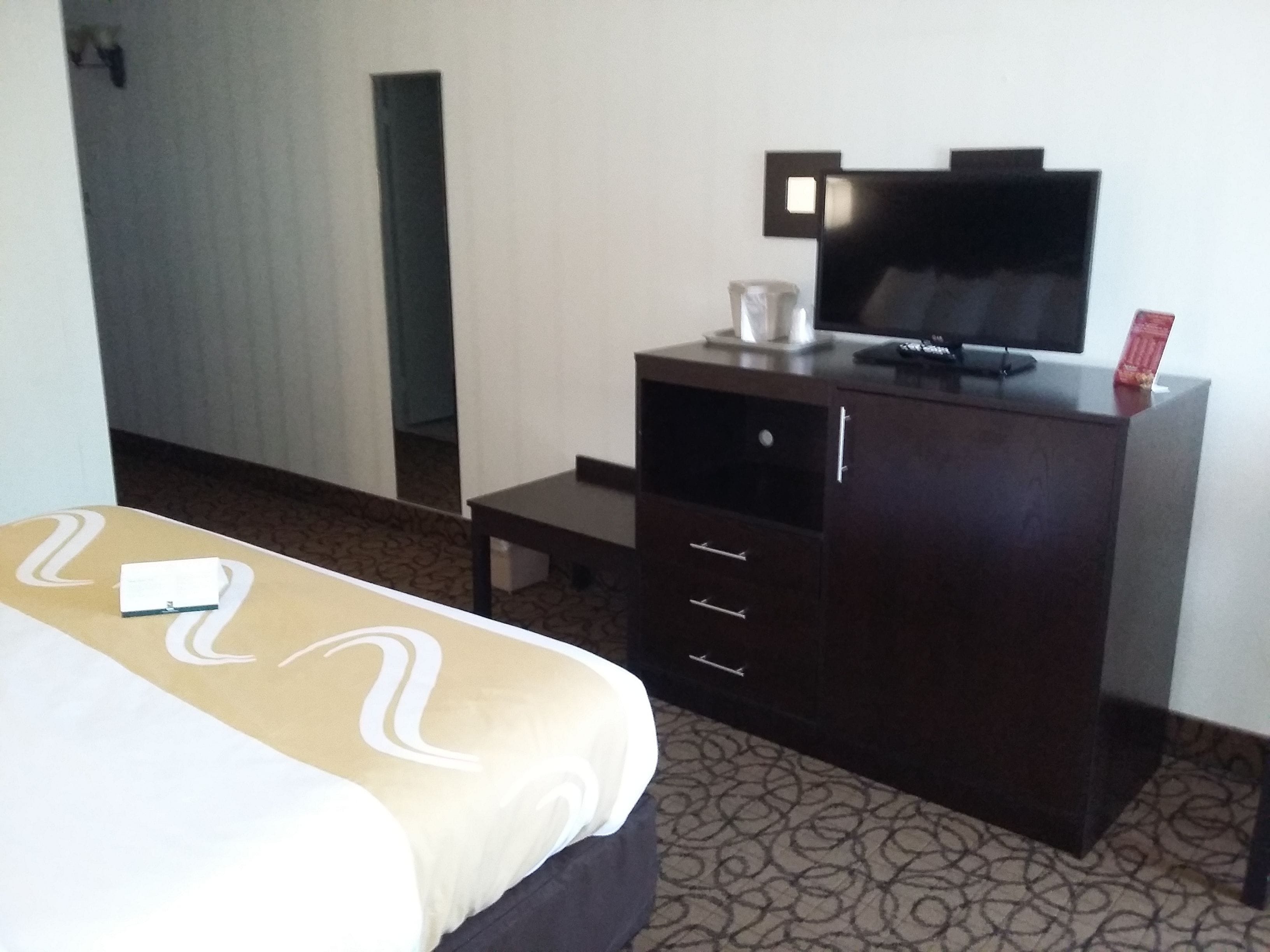 Habitació d'hotel amb un llit, un taulell de fusta fosca amb televisió i una taula petita.