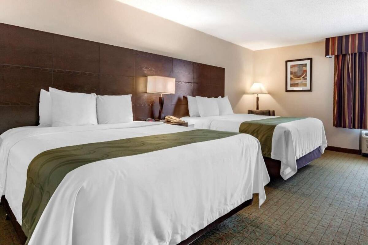 A hotel room with two beds, a headboard, bedside lamps, a telephone, and a framed picture on the wall.