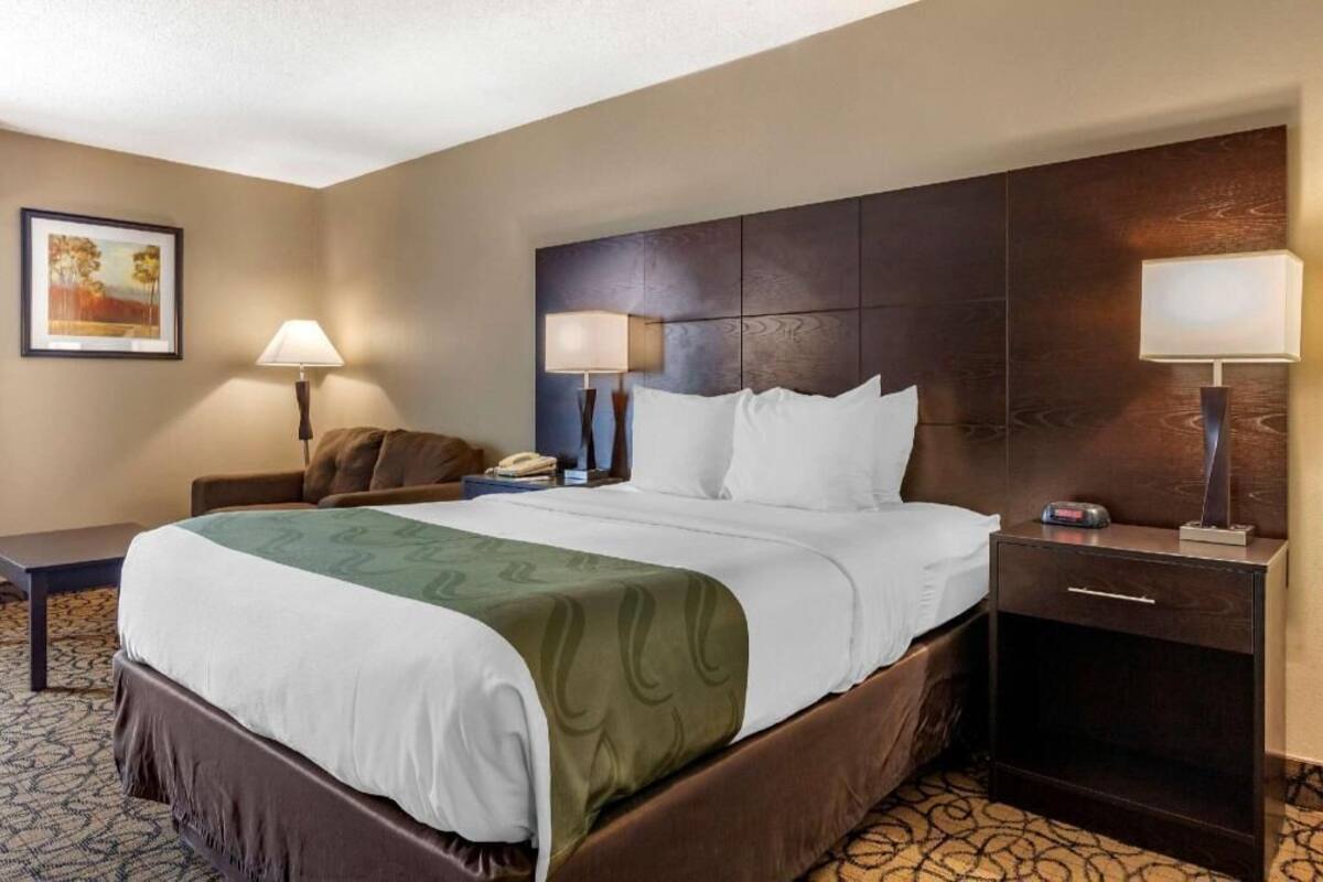 A hotel room with a bed, bedside lamps, a nightstand, and a framed picture on the wall.