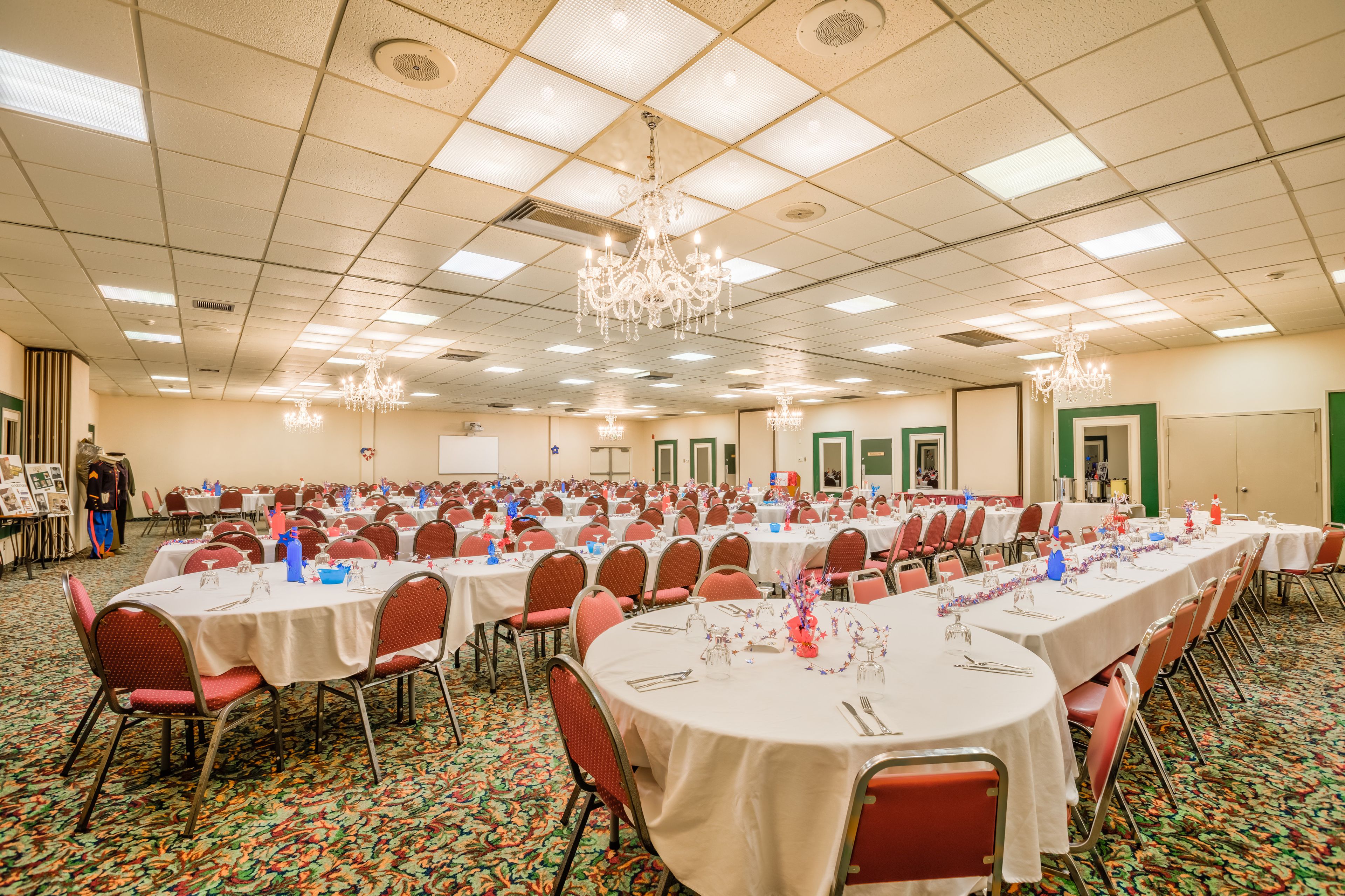 A banquet hall with multiple round tables, chairs, and chandeliers.