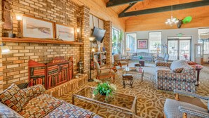 A cozy, well-lit room with a brick wall, wooden ceiling beams, a comfortable sofa, a coffee table, and a bookshelf.
