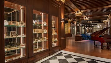 A grand lobby with wooden paneling, glass display cases, a grand piano, and a checkered floor.