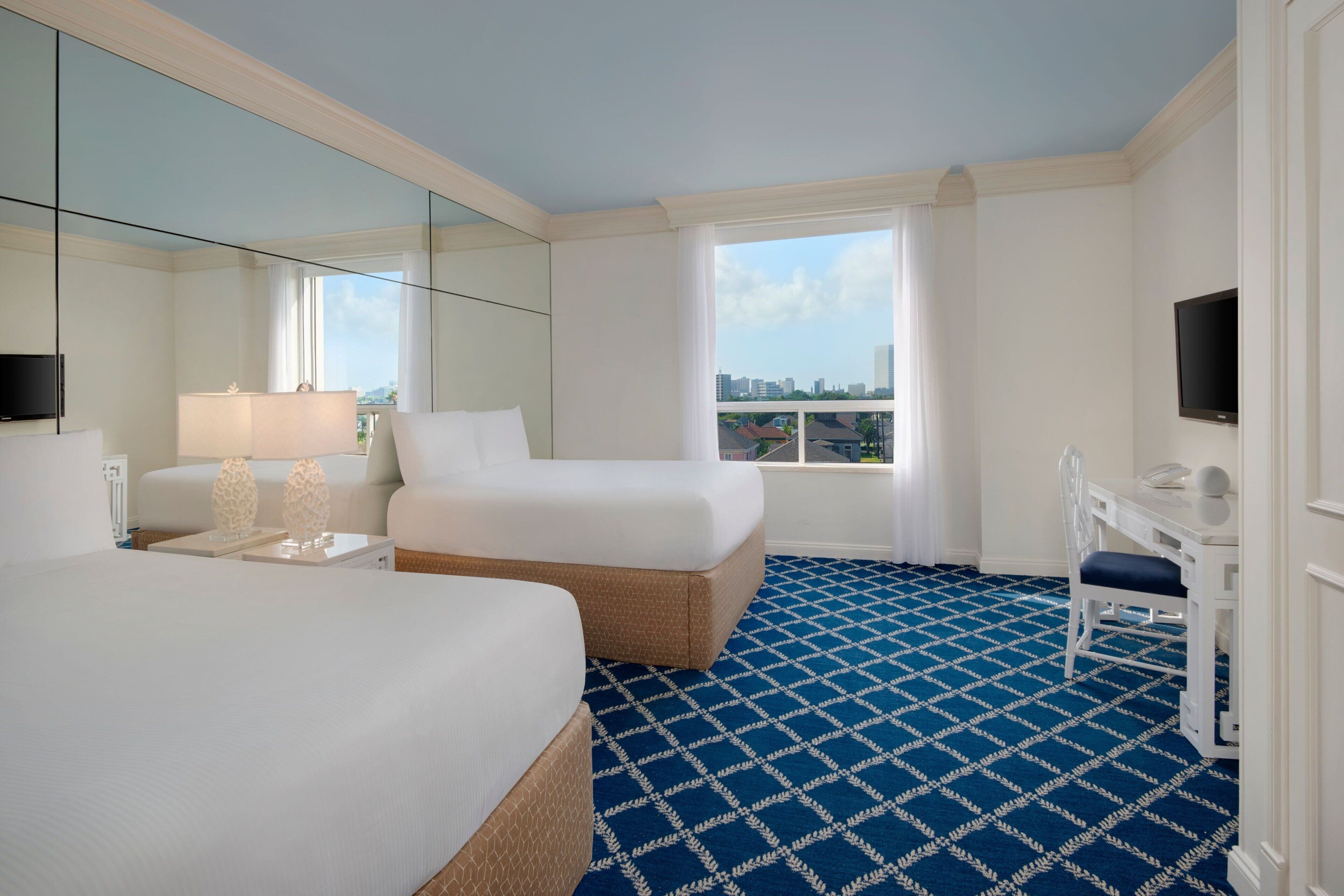 A hotel room with a large bed, a desk with a chair, a television, and a city view through the window.