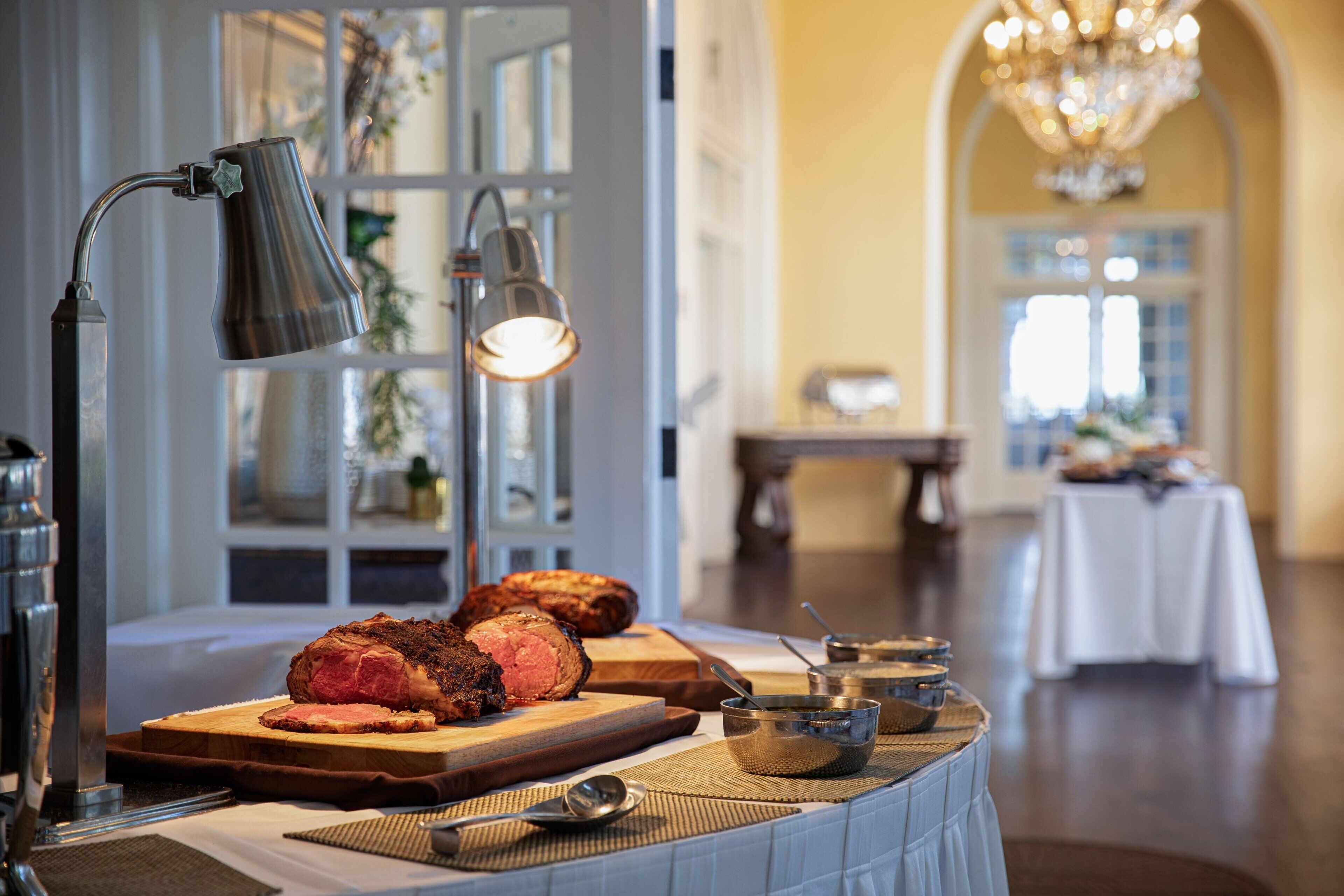 A dining area with a table set for a meal, featuring a roasted meat centerpiece, a lamp, and various serving dishes.