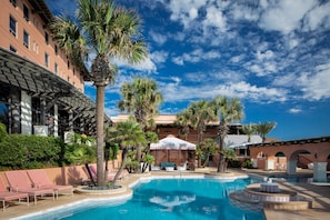 A pool area with lounge chairs, palm trees, and a building with a covered patio.
