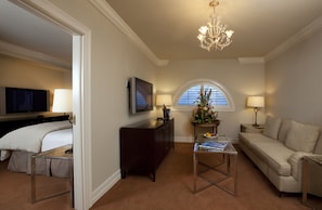 A hotel room with a bed, a sofa, a TV, a desk, and a chandelier.