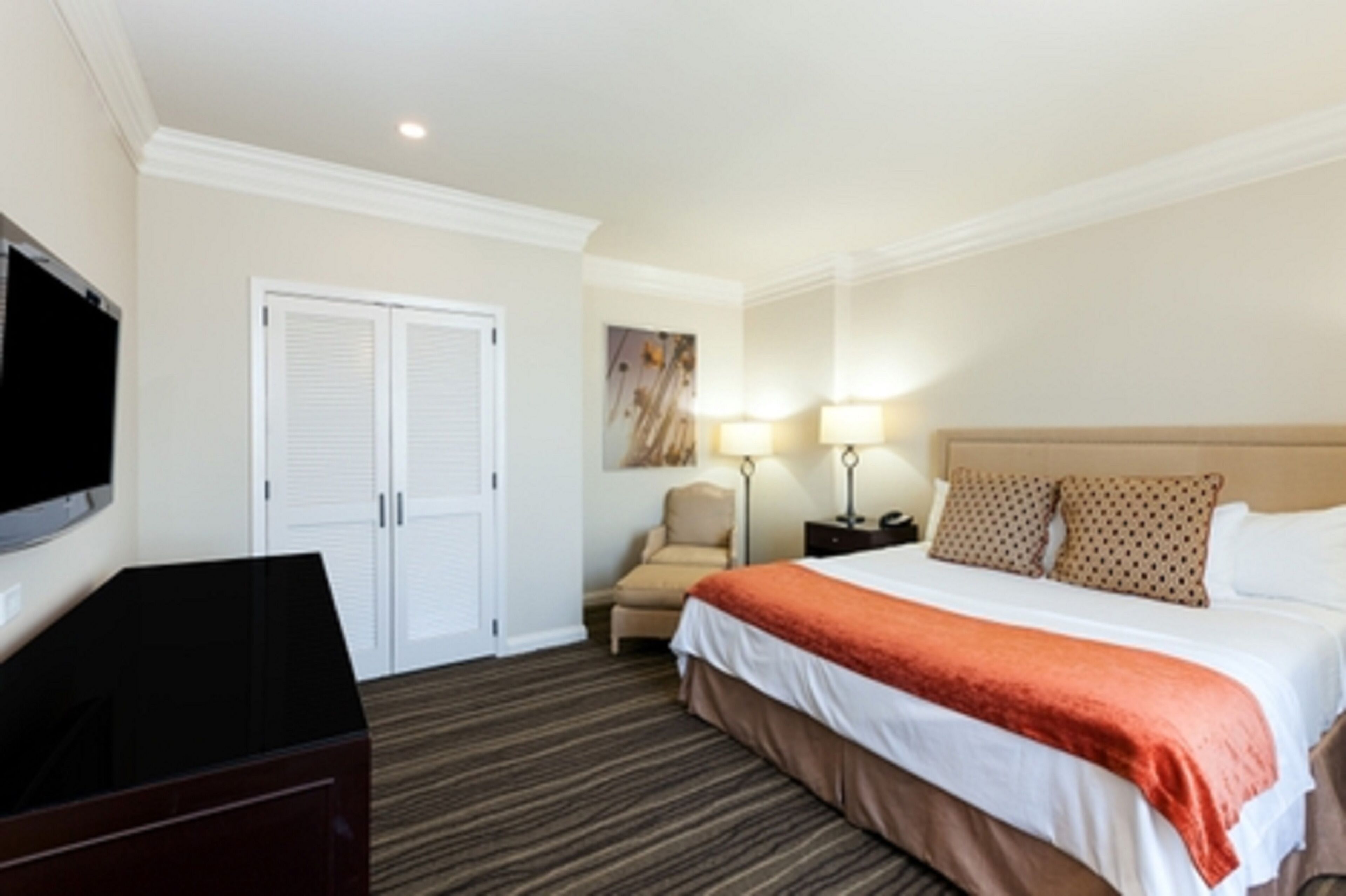 A hotel room with a bed, a TV, a chair, a desk, and a lamp.