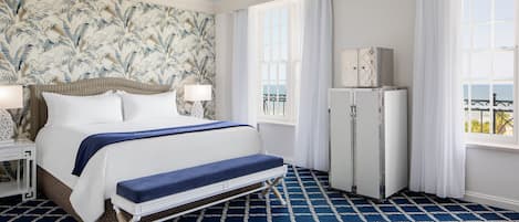 A hotel room with a large bed, a bench, a wardrobe, and a view of the sea.