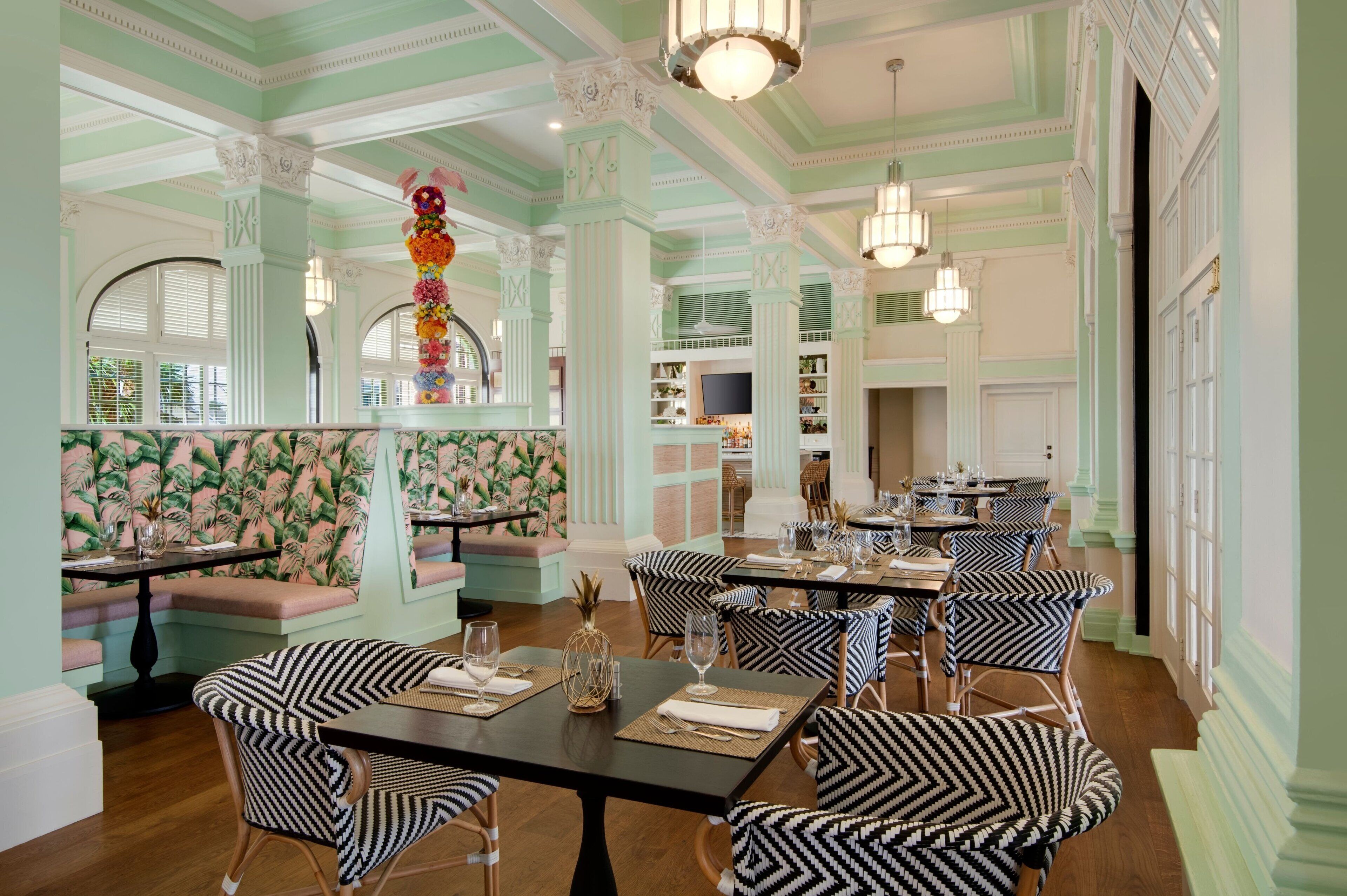 A dining area with striped ceiling, patterned wallpaper, and black and white patterned chairs.