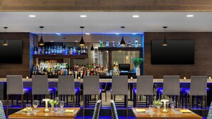 A bar area with multiple seating arrangements, a well-stocked liquor shelf, and modern pendant lighting.