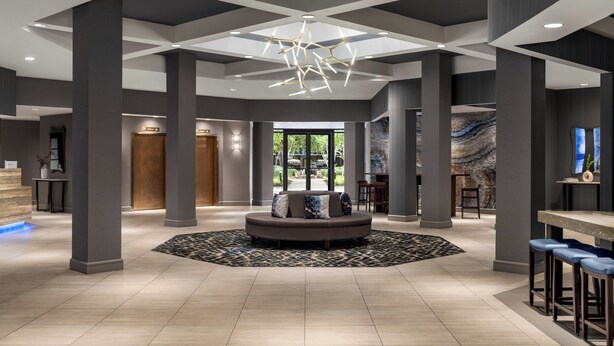 A spacious lobby with a central seating area, large pillars, and a modern chandelier.