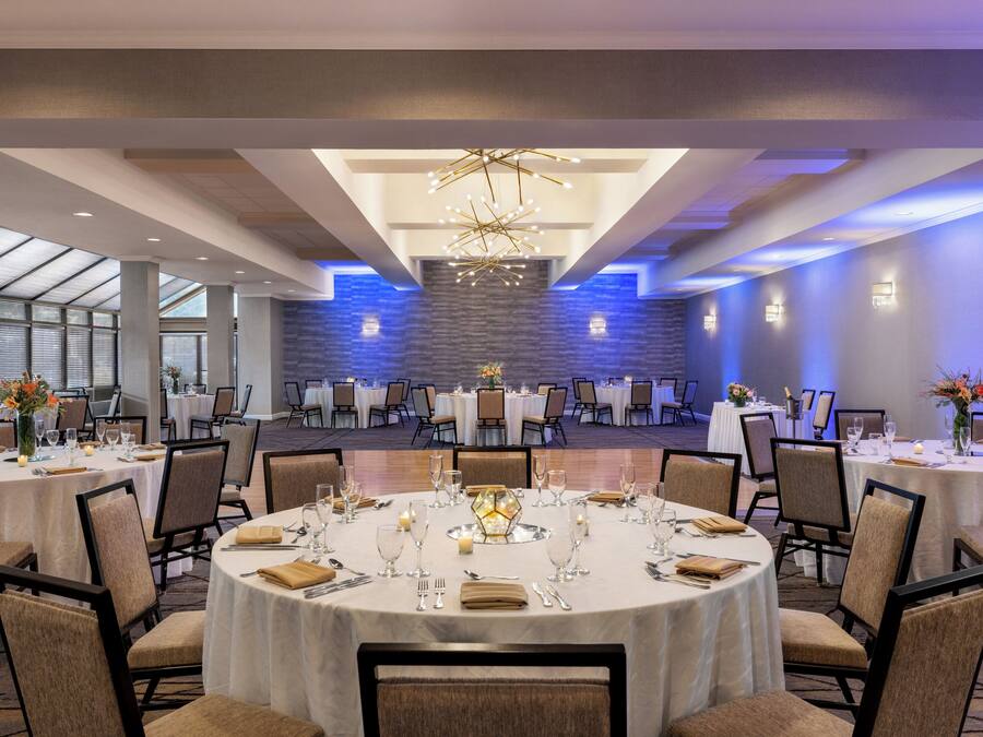 Un salón de banquetes con mesas redondas dispuestas para comer, una lámpara central y una pared de acento de piedra.