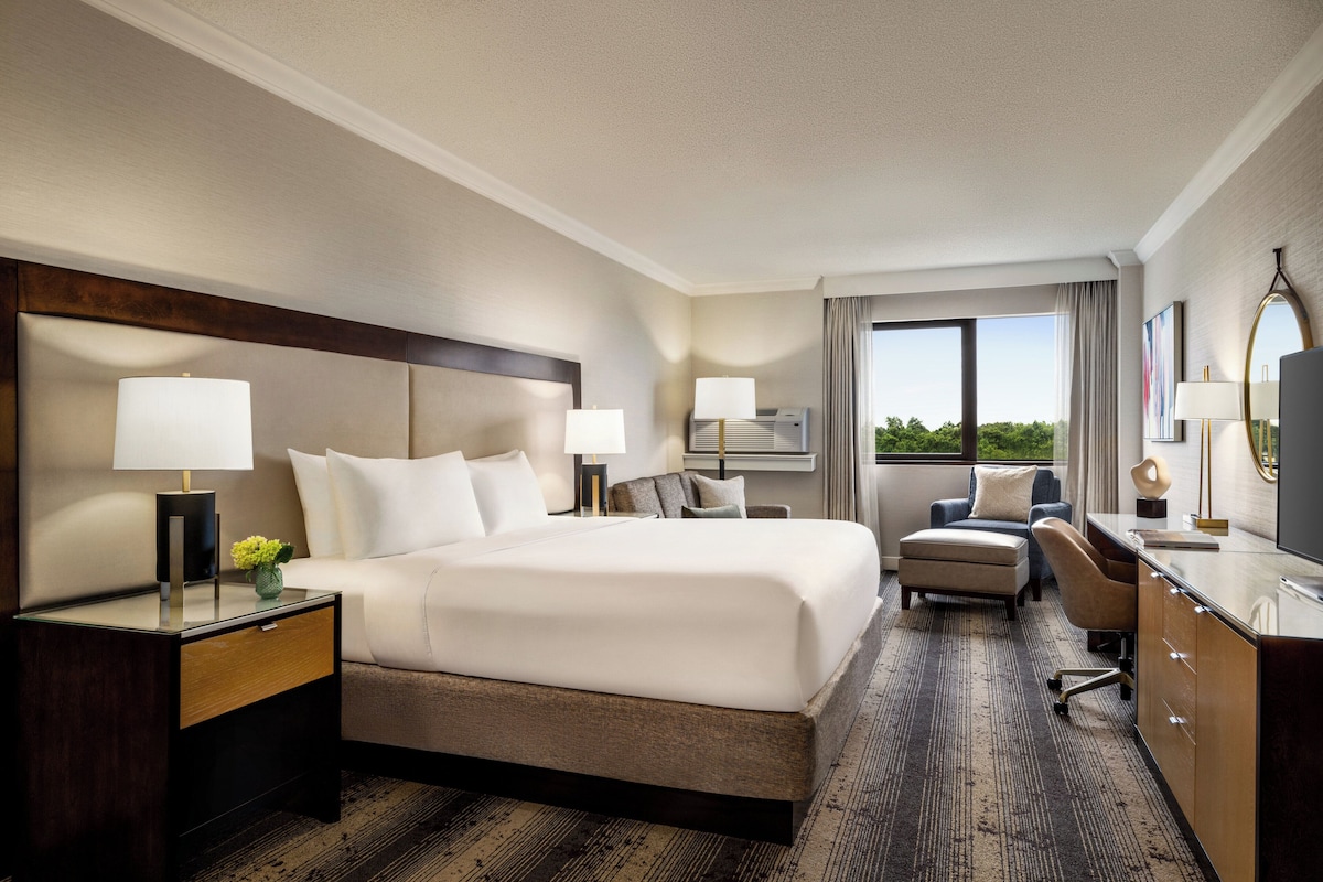 A hotel room with a large bed, bedside tables, a desk, a chair, and a view of the outdoors.