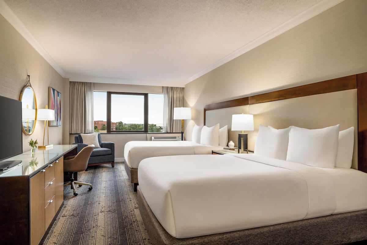 A hotel room with two beds, a desk, a chair, and a large window.