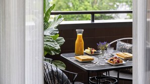 A balcony table with a breakfast setting including a glass of orange juice, a plate of fruit, a glass of water, and a small vase with flowers.