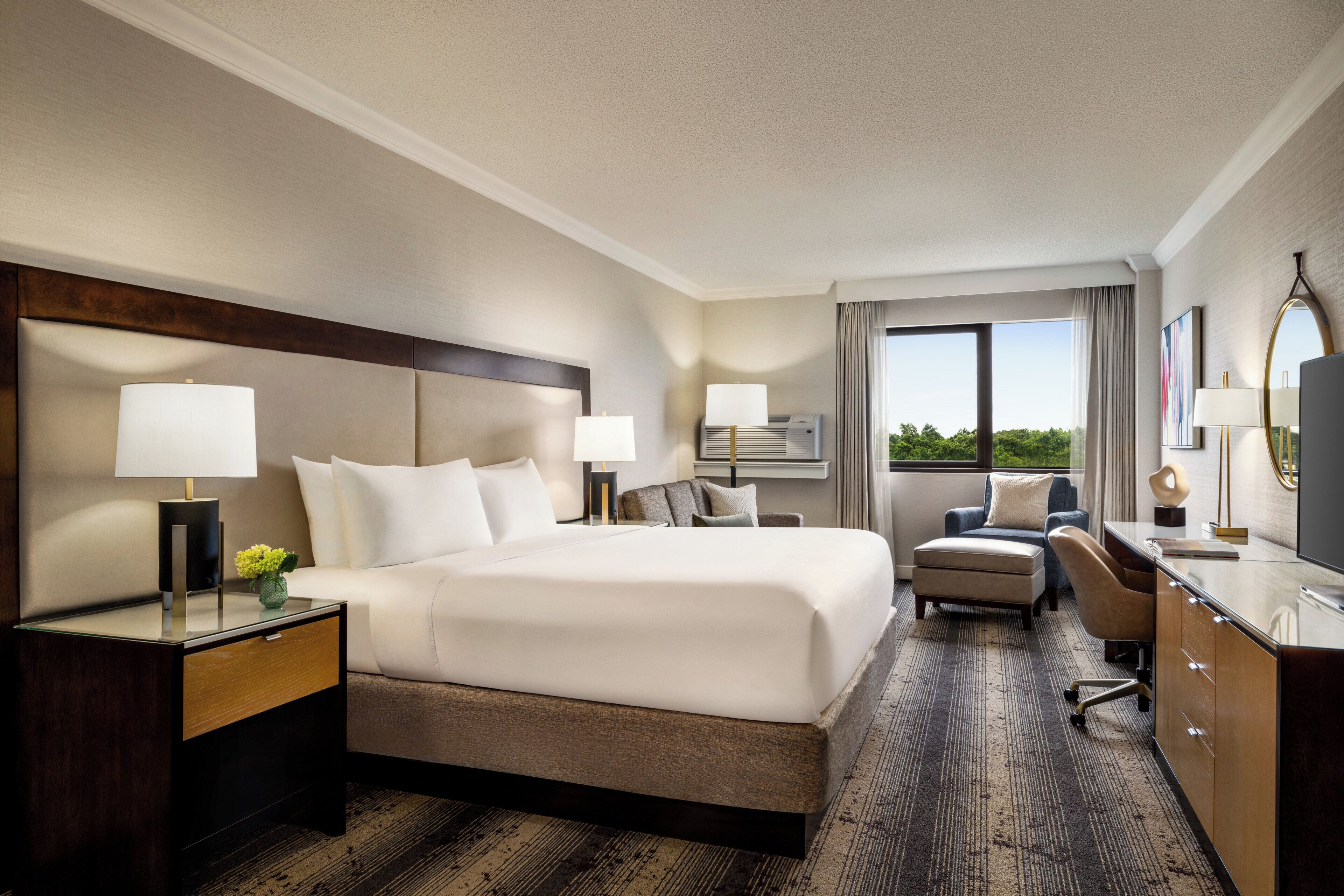 A hotel room with a large bed, bedside tables, a desk, a chair, and a view of the outdoors.