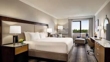 A hotel room with a large bed, bedside tables, a desk, a chair, and a view of the outdoors.