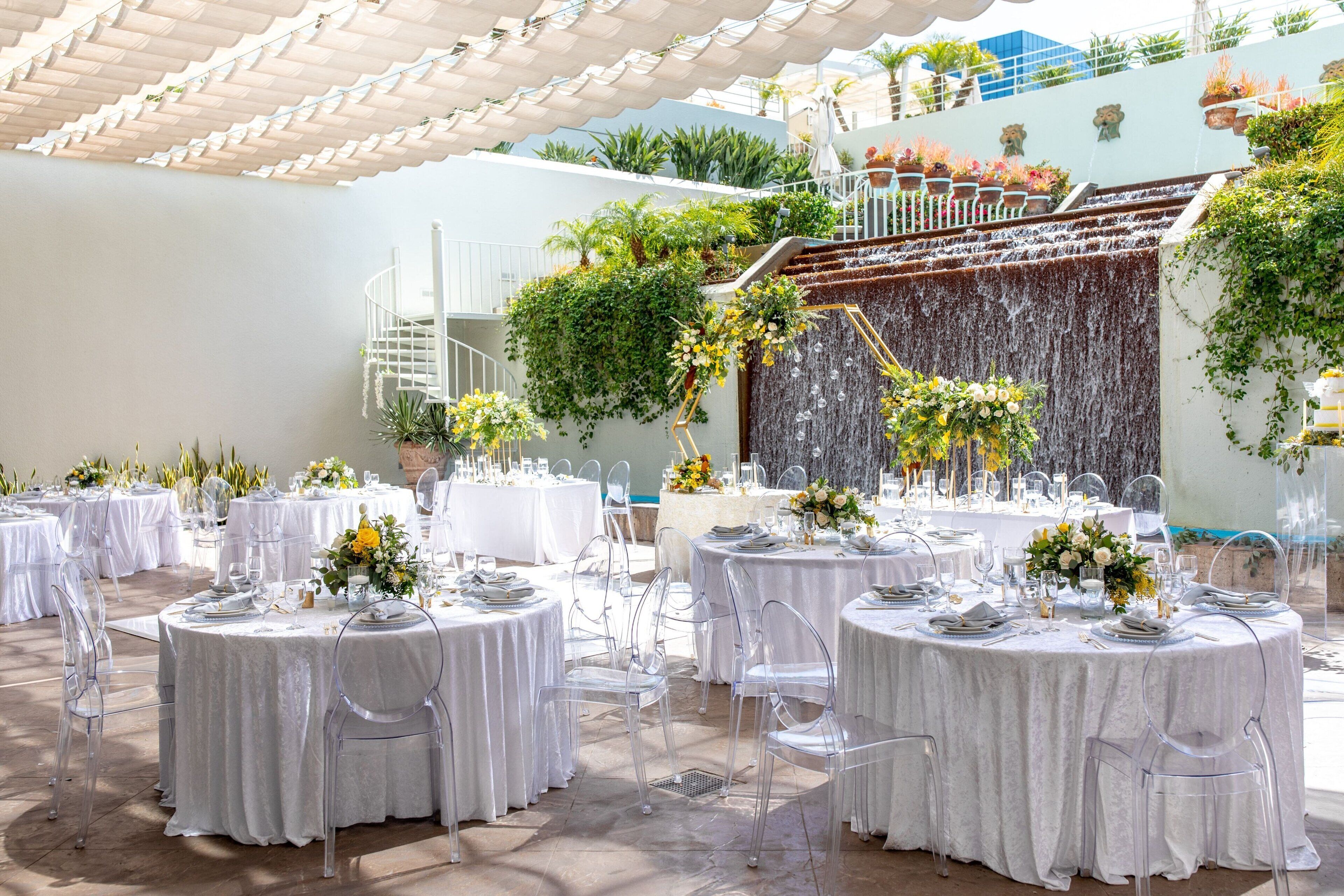 An outdoor dining area with round tables, clear chairs, and white tablecloths.