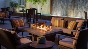 Un espacio al aire libre con mobiliario de mimbre, una chimenea y una cascada de fondo.
