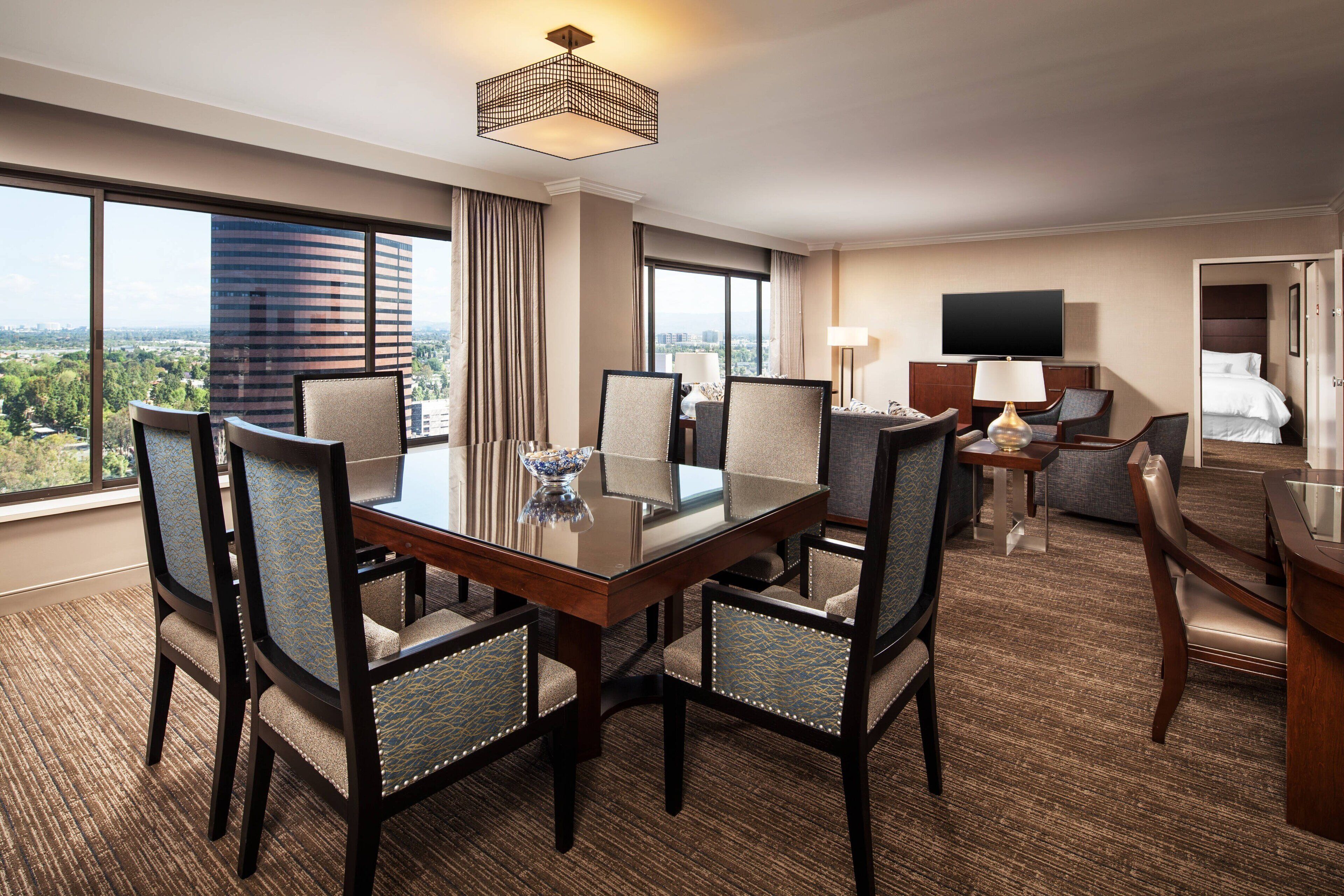 Habitación de hotel con una gran mesa de comedor, varias sillas, televisión y vistas a la ciudad.