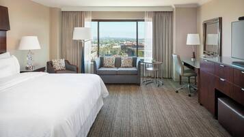 A hotel room with a large bed, a sofa, a desk, and a TV.