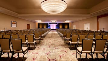 A conference room with rows of chairs, a large chandelier, and a carpeted floor.